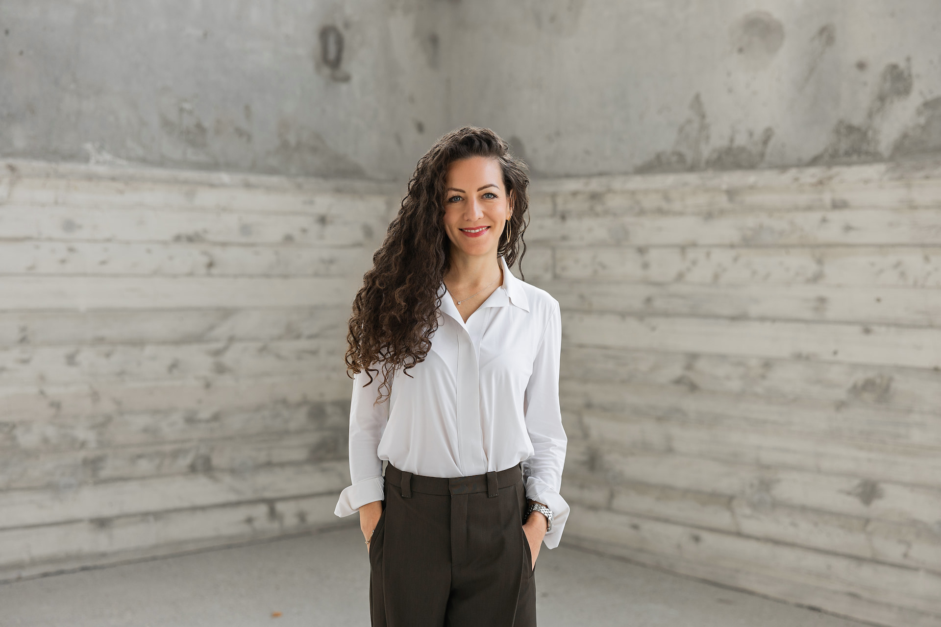 Lächelnde Frau in weissem Oberteil sitzt an einem Holztisch in einem modernen, hellen Büro – Business Portrait Fotografie Andrea Williner Zug